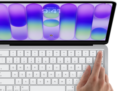 MacBook Neo, silver colour, showing login screen, person's finger on Touch ID sensor in top-right corner of keyboard